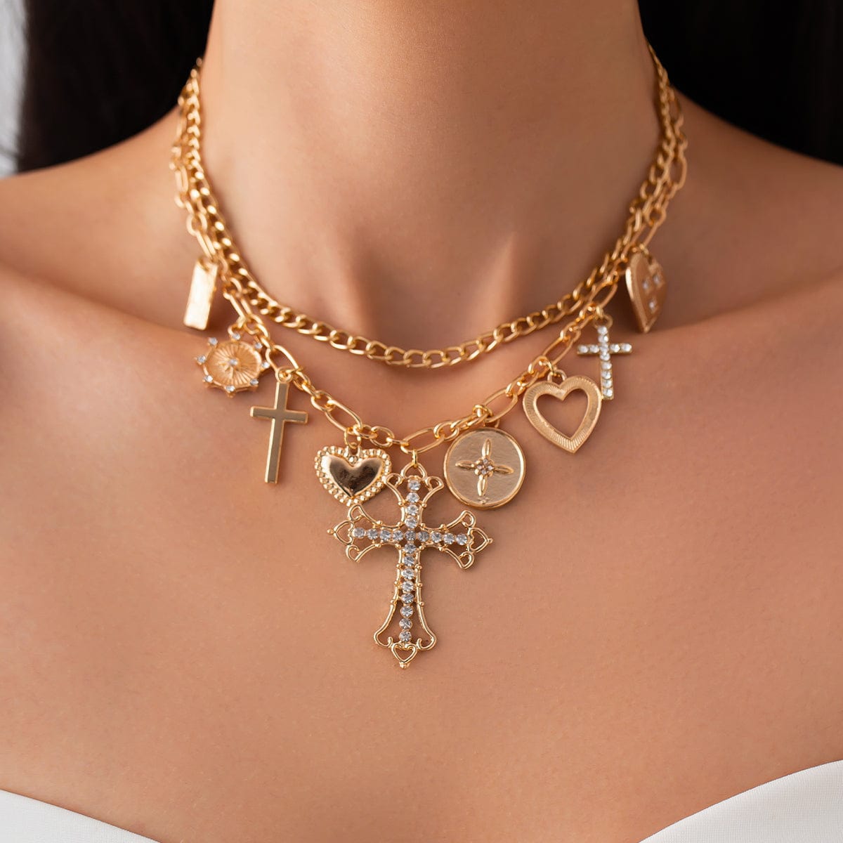 A gold-toned layered necklace with rhinestone inlaid cross and heart pendants, displayed on a model mannequin.