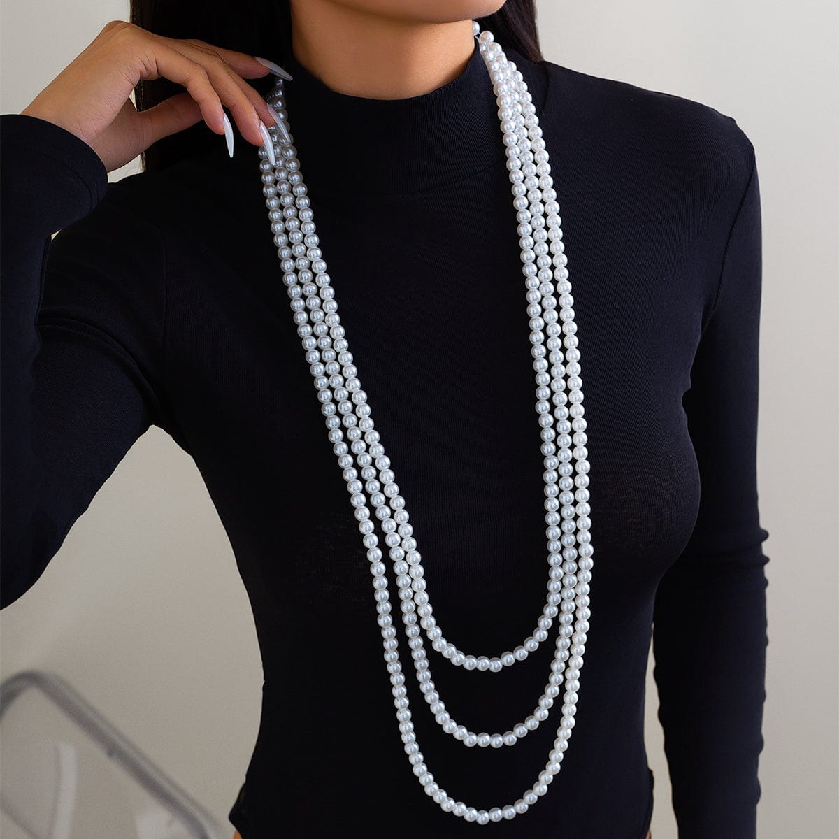 A woman wearing a black long-sleeve top and a layered pearl necklace with a long chain design.