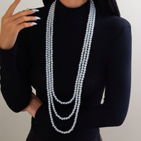 Thumbnail for A woman wearing a black long-sleeve top and a layered pearl necklace with a long chain design.