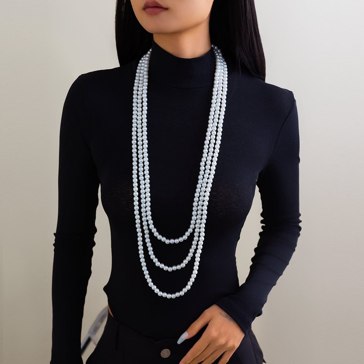 A woman wearing a black long-sleeve top and a layered pearl necklace with a long chain design.
