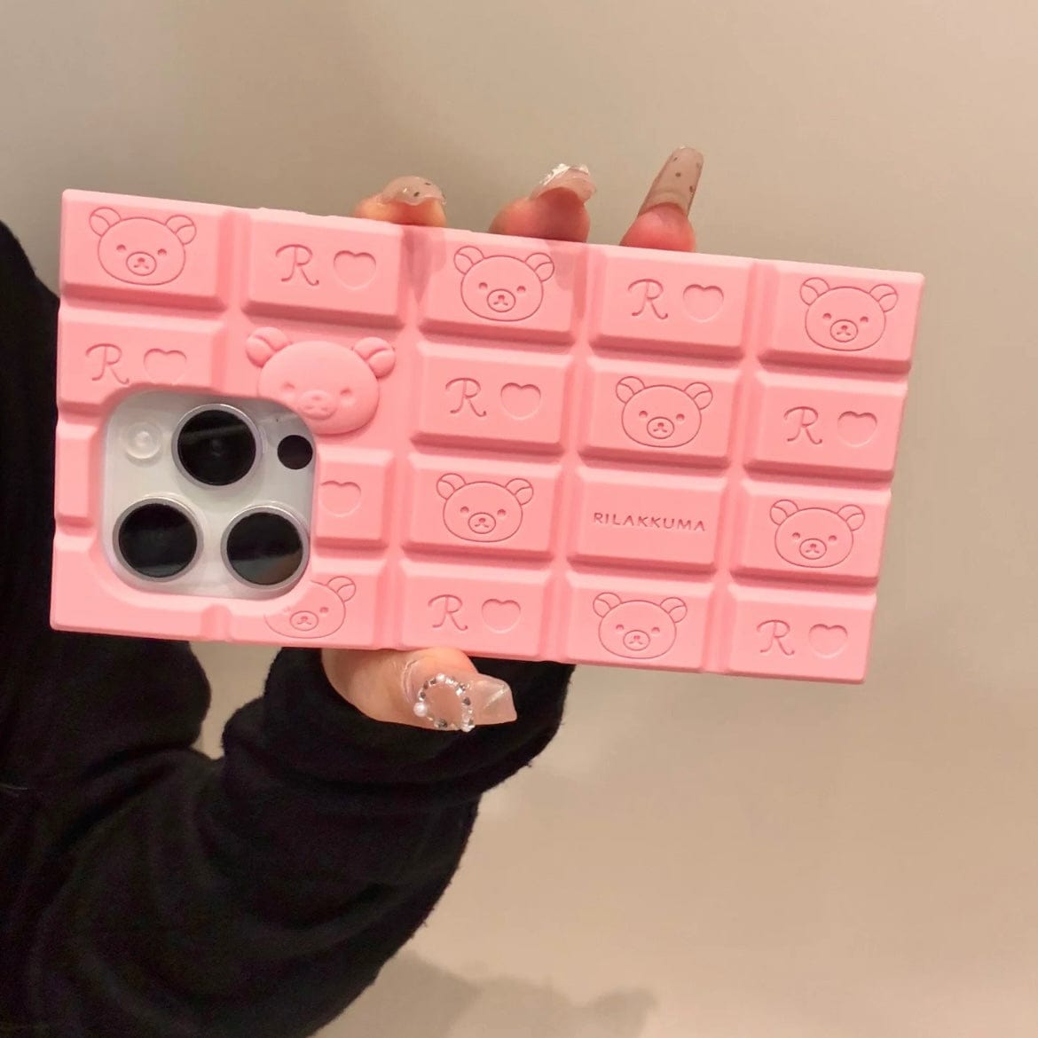 A person holding a chocolate-colored silicone iPhone case featuring Rilakkuma and Hello Kitty characters.