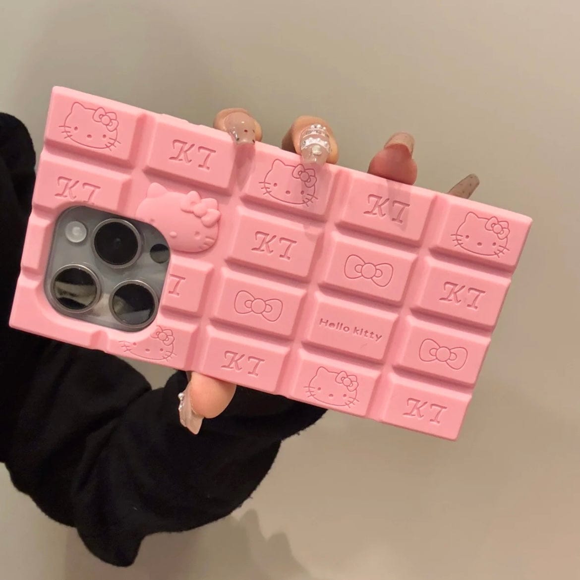 A person holding a chocolate-colored silicone iPhone case featuring Rilakkuma and Hello Kitty characters.