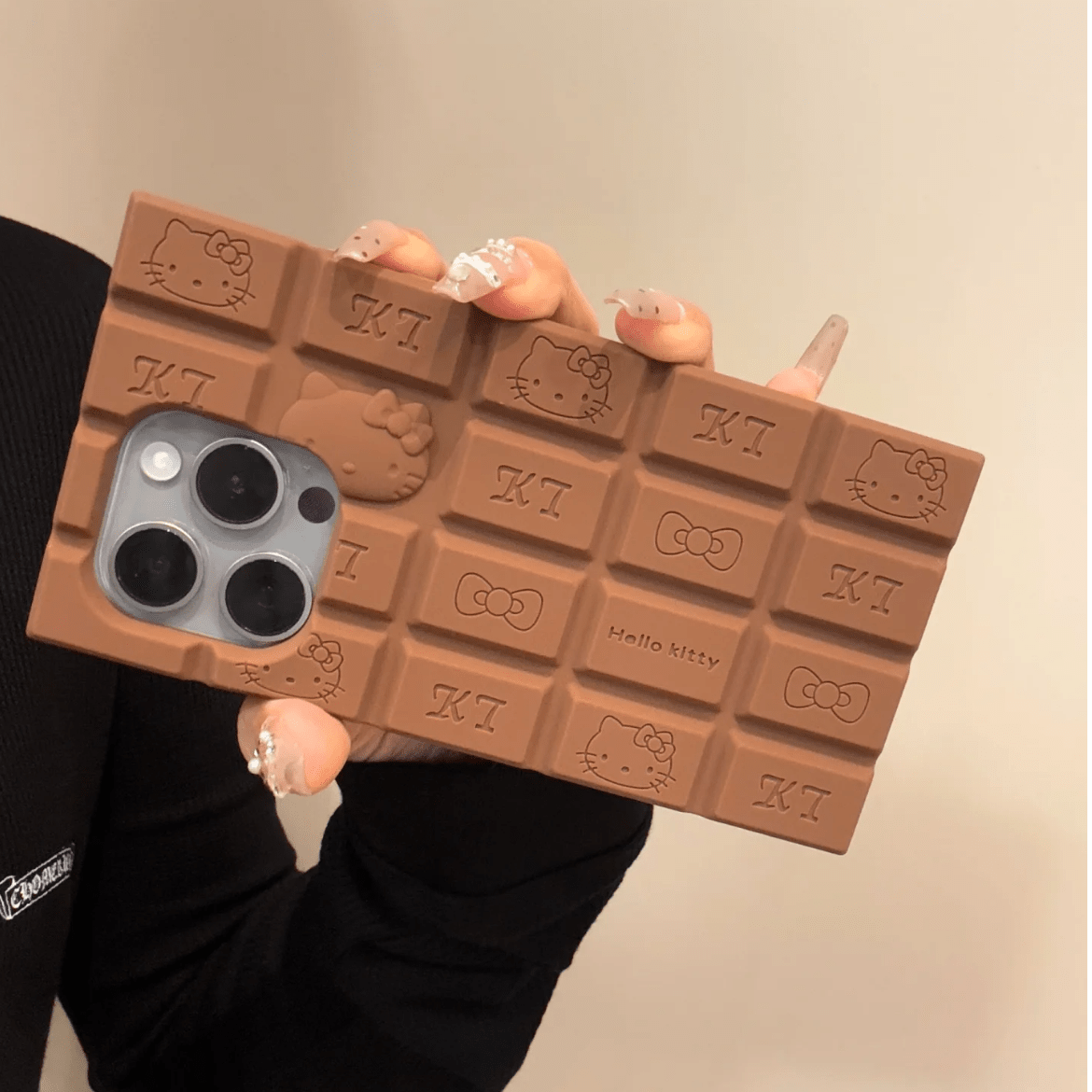 A person holding a chocolate-colored silicone iPhone case featuring Rilakkuma and Hello Kitty characters.