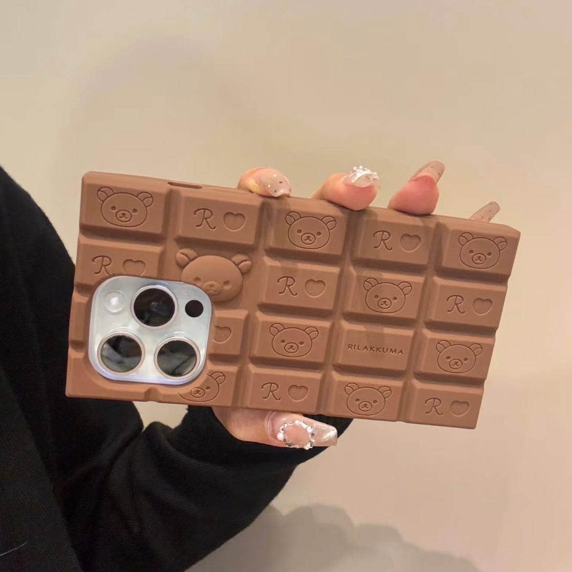 A person holding a chocolate-colored silicone iPhone case featuring Rilakkuma and Hello Kitty characters.