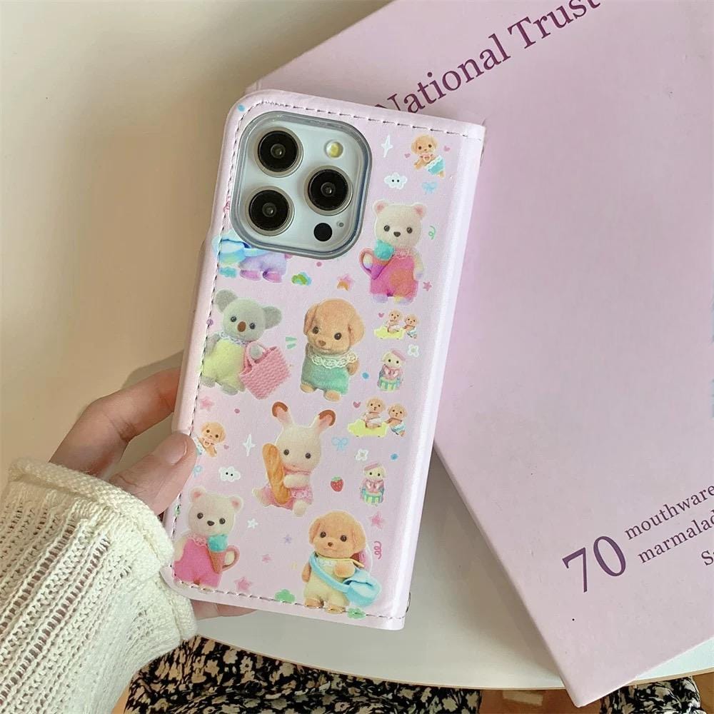 A person holding a pink iPhone case with a Sylvanian Families theme, featuring character illustrations and a small charm.