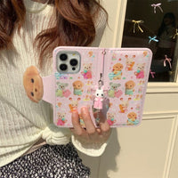 Thumbnail for A person holding a pink iPhone case with a Sylvanian Families theme, featuring character illustrations and a small charm.