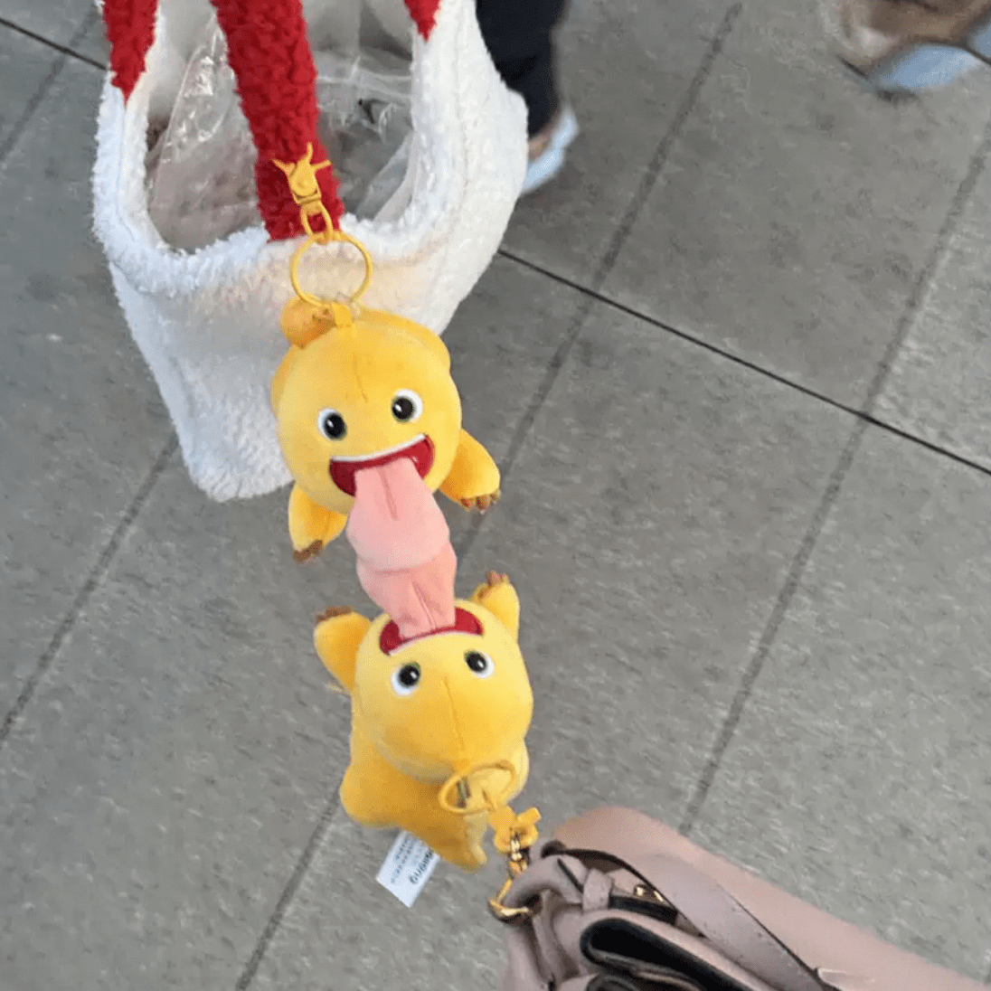 A plush dragon keychain doll with a big tongue, in yellow and pink colors, attached to a metal keychain.