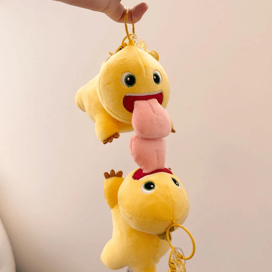A plush keychain depicting a yellow dragon with a big tongue, hanging by a metal ring.