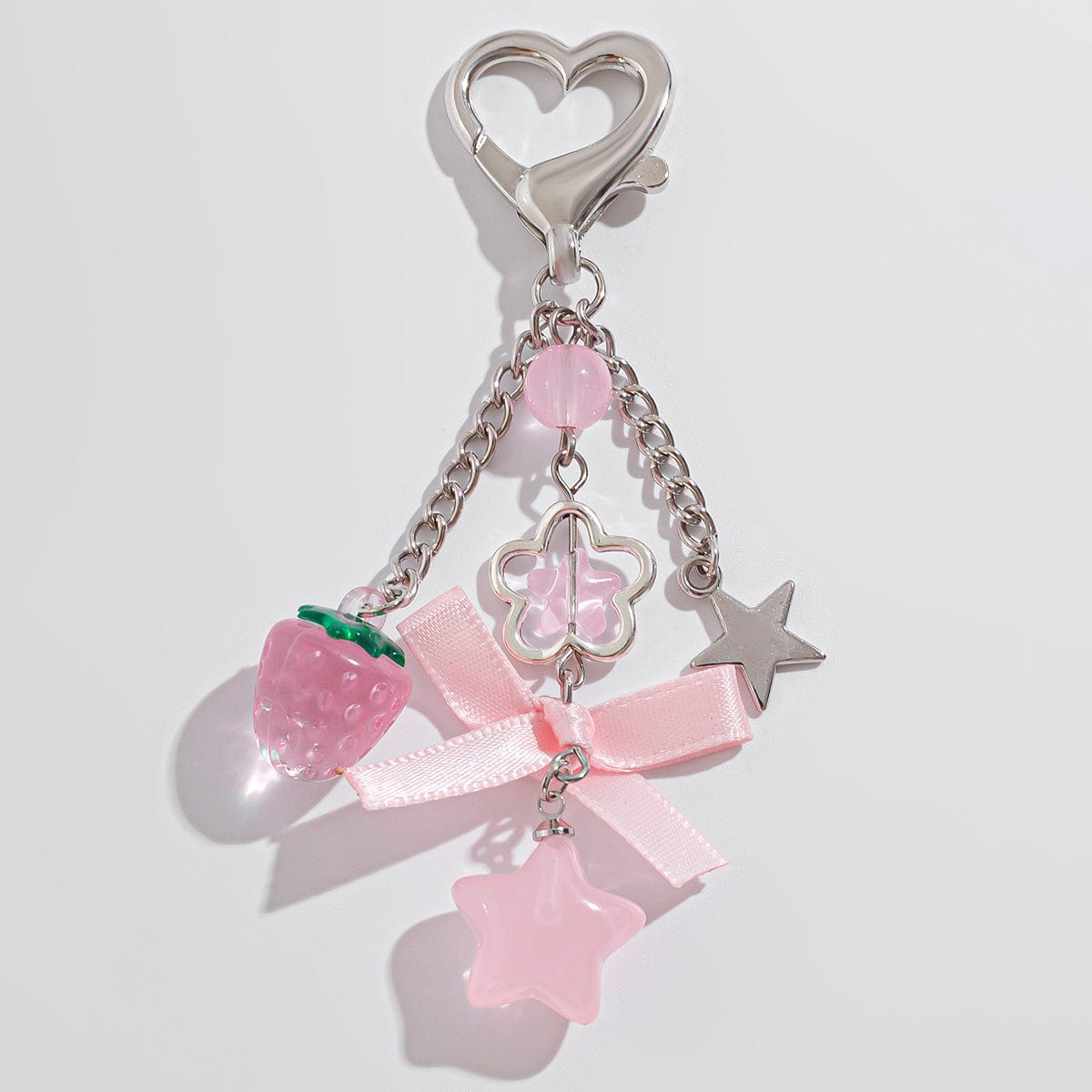 A heart-shaped keychain with a bowknot, strawberry, and star charms, in pink tones with metal accents.